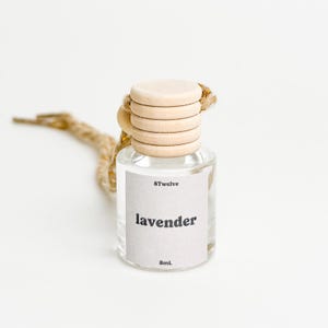 May include: A clear glass bottle with a wooden cap and a white label that says "8Twelve lavender 8mL". The bottle is hanging from a brown string.