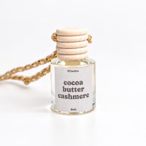 May include: A small clear glass bottle with a light wood ribbed cap and a braided hanging cord. The white label features the text 8twelve, cocoa butter cashmere, and 8mL in dark gray font. The bottle contains a clear liquid fragrance oil.
