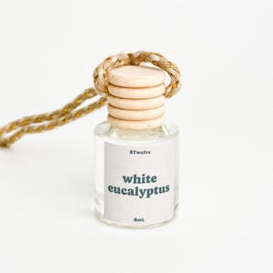 May include: A small, clear glass bottle with a wooden cap and a woven rope loop. The label reads "white eucalyptus" and "8mL". The bottle is designed to be hung, likely as an air freshener or aromatherapy product.