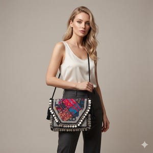 May include: A colorful patchwork crossbody bag with a black braided strap. The bag features a mix of red, blue, and purple fabrics, embellished with silver-colored coins and black tassels. The bag is worn over the shoulder.
