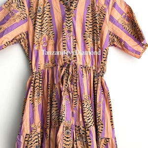 May include: A midi dress with a vertical striped pattern in peach and purple. The dress features a tiger print design and a drawstring waist. The text "TanzanitevsDiamond" is printed on the dress.