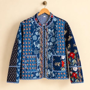 May include: A quilted jacket featuring a patchwork design in shades of blue, white, and red. The garment displays various floral, tiger, and geometric patterns, a mandarin collar, long sleeves, and two front patch pockets with blue piping.