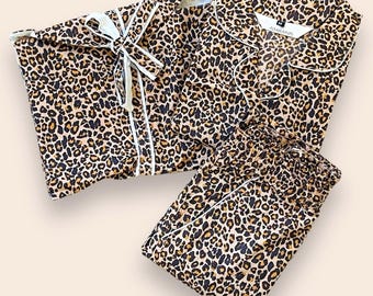 Puede incluir: Un conjunto de pijama con estampado de leopardo en tonos marrón, negro y beige. El conjunto incluye una camisa de manga larga abotonada con cuello y ribetes blancos, y un pantalón a juego con cintura elástica. La etiqueta dice AMRANIS.