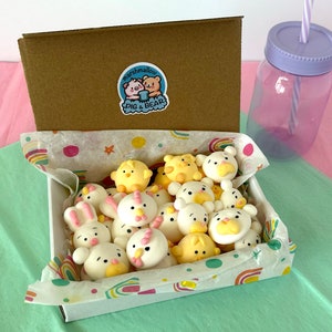 An assortment of charming marshmallow shaped like chicks, white bears, and pink-eared bunnies are presented in a box, accentuated by a colorful paper lining. A logo sticker on the box Marshmallow Pig and Bear, it delightful treat experience.