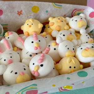 An assortment of charming marshmallow shaped like chicks, white bears, and pink-eared bunnies are presented in a box, accentuated by a colorful paper lining. A logo sticker on the box Marshmallow Pig and Bear, it delightful treat experience.