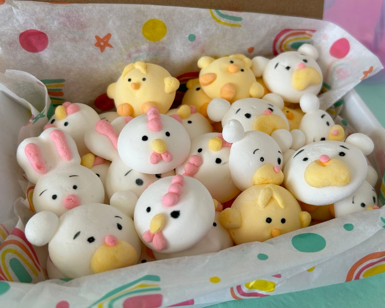 An assortment of charming marshmallow shaped like chicks, white bears, and pink-eared bunnies are presented in a box, accentuated by a colorful paper lining. A logo sticker on the box Marshmallow Pig and Bear, it delightful treat experience.