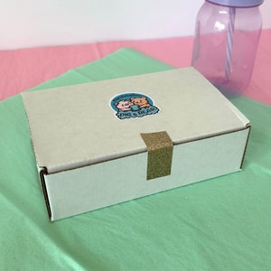 An assortment of charming marshmallow shaped like chicks, white bears, and pink-eared bunnies are presented in a box, accentuated by a colorful paper lining. A logo sticker on the box Marshmallow Pig and Bear, it delightful treat experience.