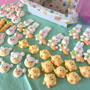 An assortment of charming marshmallow shaped like chicks, white bears, and pink-eared bunnies are presented in a box, accentuated by a colorful paper lining. A logo sticker on the box Marshmallow Pig and Bear, it delightful treat experience.