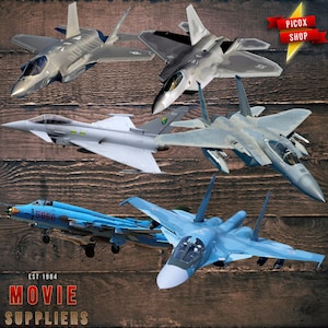 May include: A collection of military fighter jets in various colors, including gray, blue, and silver, against a wood-grain background. The image includes the text "PICX SHOP" and "MOVIE SUPPLIERS EST 1984".