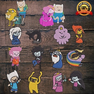 Puede incluir: Colecci&oacute;n de parches bordados con personajes de la serie animada Adventure Time. Los parches muestran varios personajes en colores vibrantes, incluyendo a Finn, Jake, Princesa Chicle y otros, con costuras detalladas sobre un fondo de madera.