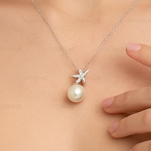 May include: A silver necklace with a starfish pendant, adorned with small, clear stones, and a large, round, white pearl. The necklace is displayed around the neck, highlighting the intricate design and elegant style.