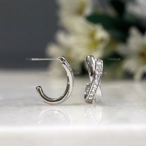 以下が含まれることがあります： クロスデザインとクリアなキュービックジルコニアの石が付いたシルバーのフープイヤリングのペアです。