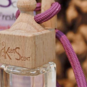 May include: A small glass bottle with a wooden lid and a purple string. The bottle has a label that says "Kube Scent".