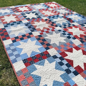 May include: A quilt featuring a repeating pattern of large white stars set against a background of red, white, and blue checkered and patterned fabric squares. The text BETTY QUILT PATTERN NO. 106 and doman design are printed on the image.