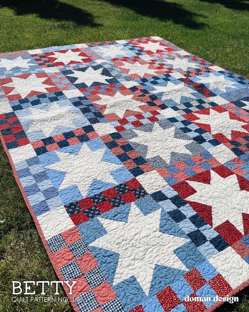 May include: A quilt featuring a repeating pattern of large white stars set against a background of red, white, and blue checkered and patterned fabric squares. The text BETTY QUILT PATTERN NO. 106 and doman design are printed on the image.