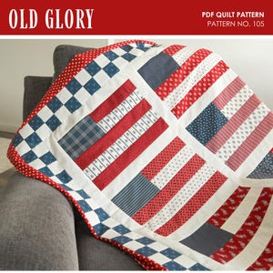 May include: A patriotic quilt with a red, white, and blue color scheme, draped over a gray armchair. The quilt features a patchwork design with stripes and squares, resembling the American flag. The text "OLD GLORY" and "PDF QUILT PATTERN PATTERN NO. 105" are visible.