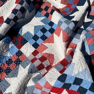 May include: A patchwork quilt featuring a repeating star pattern in white, red, and various shades of blue. The design incorporates checkered and floral fabric squares with intricate quilted stitching throughout. Text reads BETTY QUILT PATTERN NO 106.