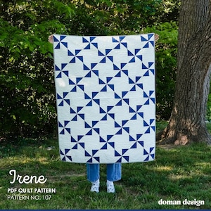 May include: A white and blue quilt with a geometric pattern of blue triangles arranged in a pinwheel design. The quilt is held up in front of a person. The text "Irene PDF Quilt Pattern Pattern No. 107" is visible.