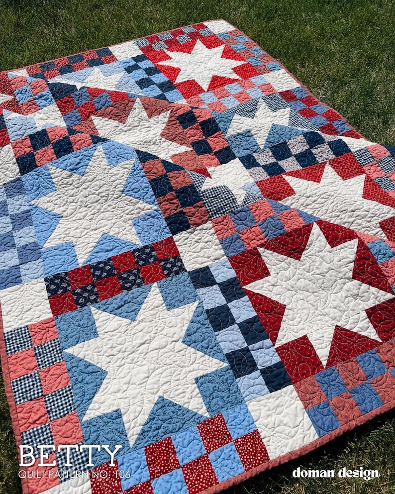 May include: A quilt featuring a repeating pattern of large white eight-pointed stars set against a background of red, white, and blue checkered and patterned fabric squares. The quilt has a visible stippled quilting texture and text reading BETTY QUILT PATTERN NO. 106 and doman design.