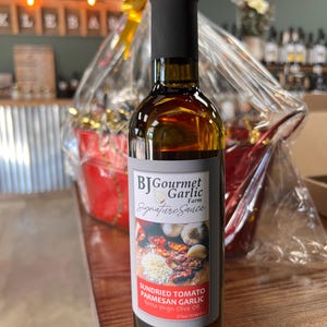May include: A clear glass bottle of BJ Gourmet Garlic Farm Signature Sauce. The label features images of sundried tomatoes, Parmesan cheese, and garlic. The bottle is filled with a dark liquid and topped with a black cap. The bottle contains 375ml (12.68 fl oz).