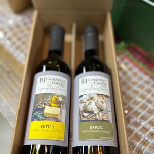 May include: Two glass bottles of BJ Gourmet Garlic Signature Sauce in a cardboard box. One bottle is labeled "Butter Extra Virgin Olive Oil", the other "Garlic Dark Balsamic Vinegar". Each bottle contains 375ml (12.68 fl oz).