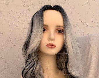 May include: A long, wavy wig with black and silver streaks. The wig is styled with loose waves and is worn on a mannequin head.