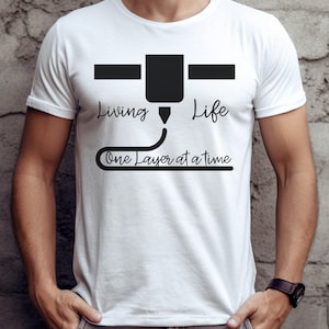 May include: White t-shirt with a black 3D printer graphic and the text "Living Life One Layer at a Time".