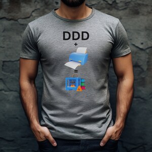 Pode incluir: Uma camiseta cinza com o texto "DDD + =" e uma ilustra&ccedil;&atilde;o de uma impressora e uma impressora 3D.