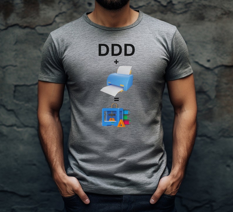 Pode incluir: Uma camiseta cinza com o texto "DDD + =" e uma ilustra&ccedil;&atilde;o de uma impressora e uma impressora 3D.