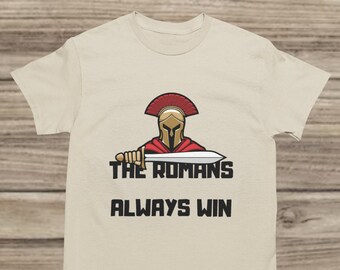May include: A beige t-shirt with a graphic of a Roman soldier holding a sword. The text "THE ROMANS ALWAYS WIN" is printed below the graphic.