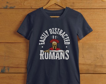 May include: A navy blue t-shirt with a white graphic of a Roman soldier with the text "Easily Distracted By Romans".