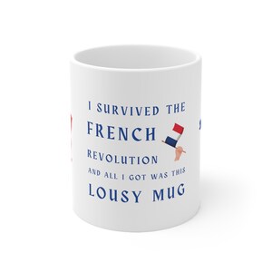 May include: White ceramic mug with blue text that reads "I survived the French Revolution and all I got was this lousy mug". The mug has a small image of a hand holding a French flag.