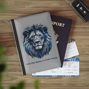 May include: A grey passport holder featuring a blue lion design and the text "WE'RE BUILT FOR THIS", alongside a passport and two boarding passes. A car key is also visible.
