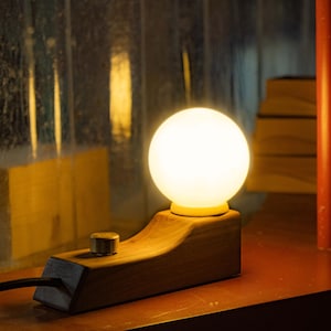 May include: A wooden table lamp with a white globe light bulb. The lamp has a simple design and a brown wooden base with a knob switch.