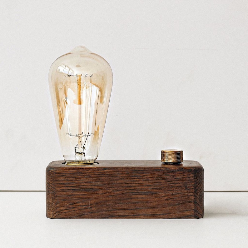 May include: A wooden lamp base with a brass knob switch and a vintage-style light bulb. The lamp is made of dark wood and has a simple, modern design.