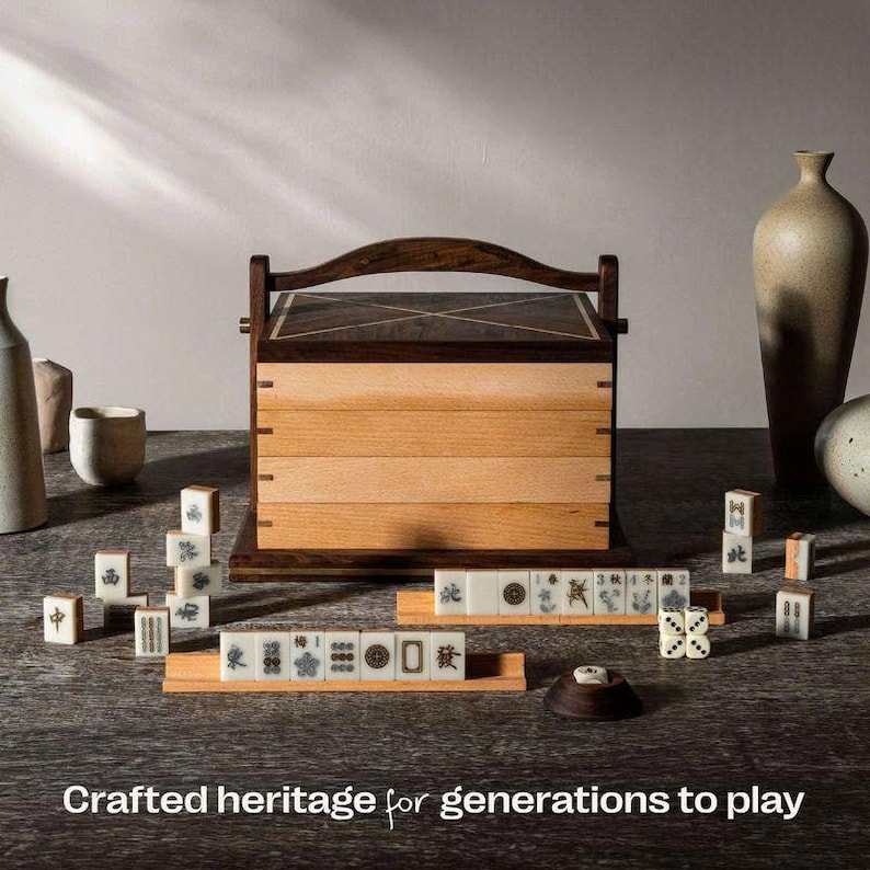 May include: A wooden Mahjong set with a two-tone wooden box and tiles. The box has a dark wood top and handle, with a lighter wood body. The tiles are white with black symbols. The text "Crafted heritage for generations to play" is at the bottom.