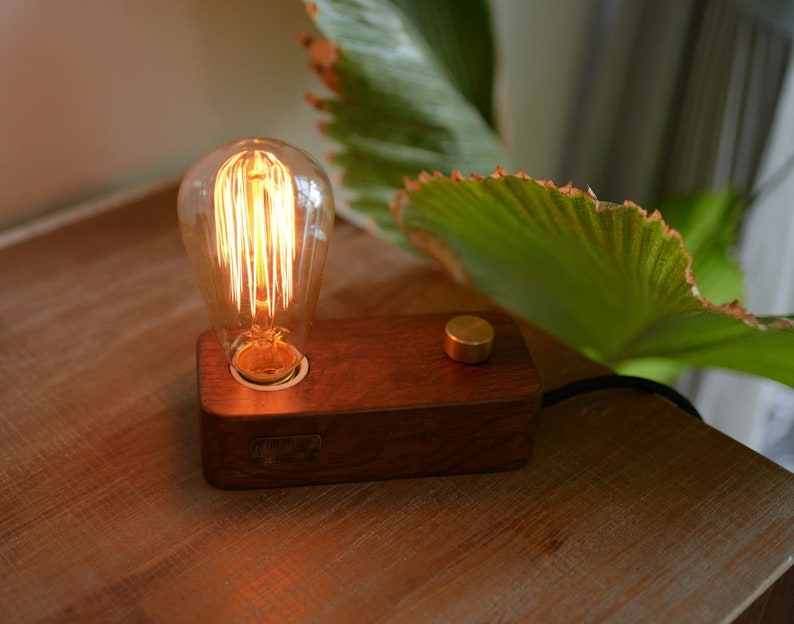 May include: A wooden table lamp with a warm, glowing Edison bulb. The lamp has a simple design with a dark wood base and a brass switch.