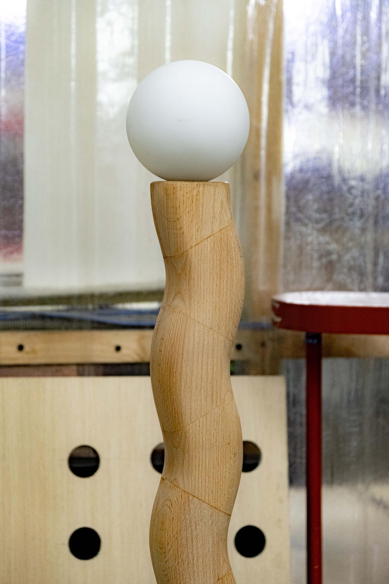 May include: A white sphere sits atop a wooden, curved pedestal. The pedestal is made of light brown wood with a smooth, polished finish.