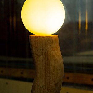 May include: A wooden lamp with a curved base and a round, glowing, white lightbulb.