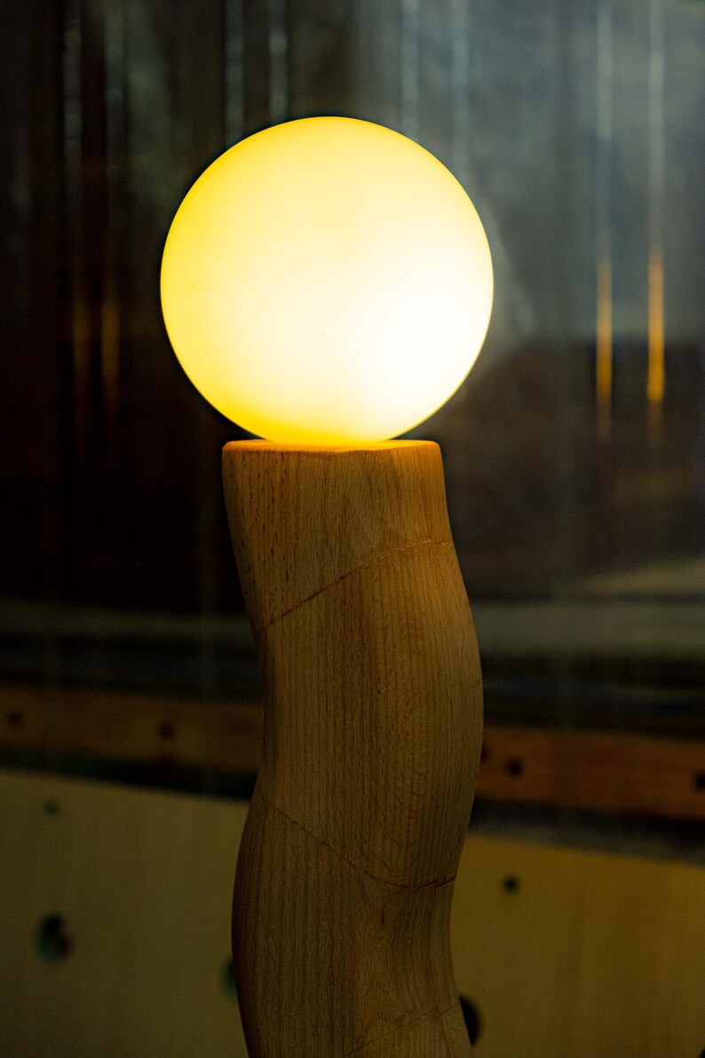 May include: A wooden lamp with a curved base and a round, glowing, white lightbulb.