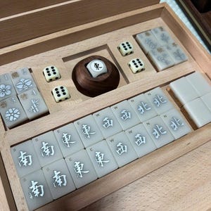 May include: A wooden Mahjong set with ivory-colored tiles and dice. The tiles feature Chinese characters and symbols. The set includes a wooden tile holder and dice with black dots. The set is neatly arranged inside a wooden box.
