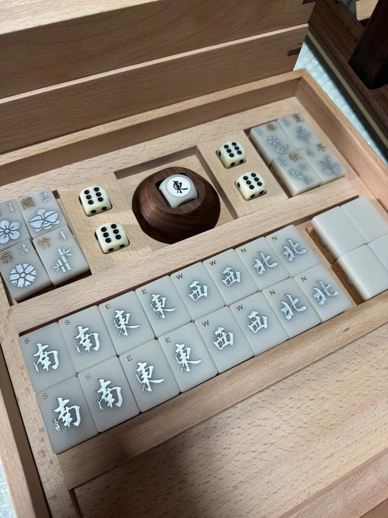 May include: A wooden Mahjong set with ivory-colored tiles and dice. The tiles feature Chinese characters and symbols. The set includes a wooden tile holder and dice with black dots. The set is neatly arranged inside a wooden box.