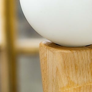 May include: A white globe-shaped lampshade sits atop a wooden base. The base is made of light brown wood with a natural grain pattern.