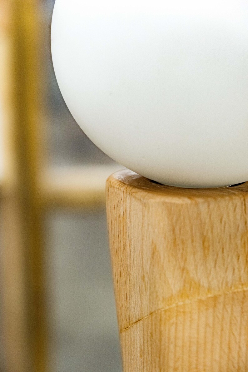 May include: A white globe-shaped lampshade sits atop a wooden base. The base is made of light brown wood with a natural grain pattern.