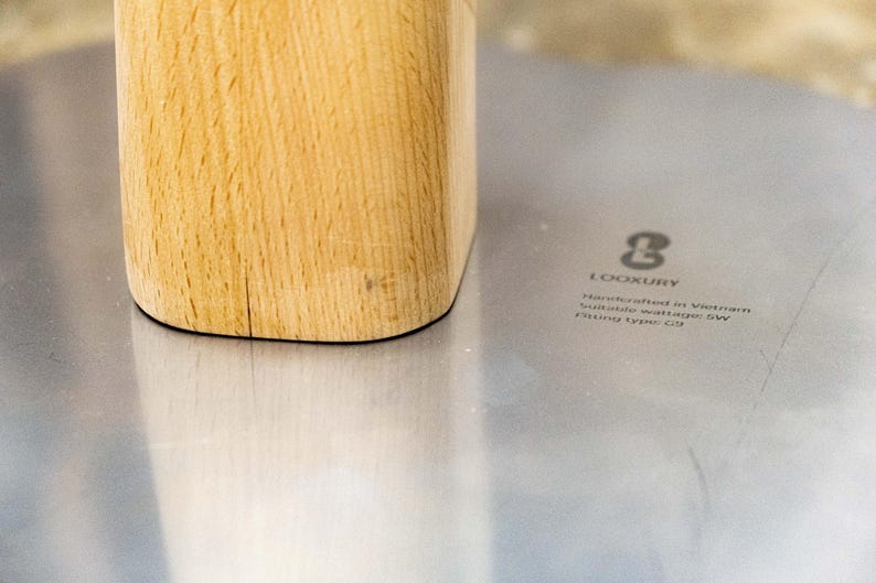 May include: Close-up of a wooden base with a light wood grain. The base is sitting on a silver surface with the text "LOOKURY Handmade in Vietnam Suitable material for SW Fitting Type: C18"