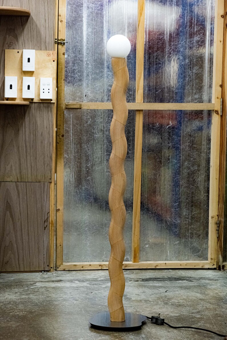 May include: A wooden floor lamp with a white globe shade. The lamp has a unique, wavy design and a black base.