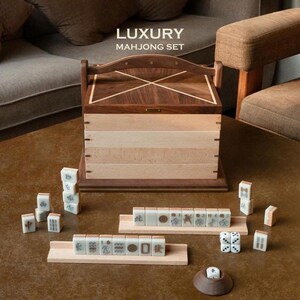 May include: A luxury Mahjong set with a wooden box and tiles. The box is made of dark and light wood, with the text "LUXURY MAHONG SET" on top. The tiles are white with black symbols. The set includes dice and wooden tile holders.