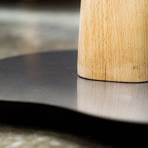 May include: A close-up of a wooden base with a gray, round surface. The base is made of light wood with a natural grain pattern.