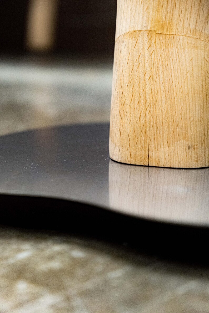 May include: A close-up of a wooden base with a gray, round surface. The base is made of light wood with a natural grain pattern.