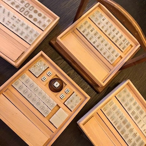 May include: Four wooden boxes containing a traditional Mahjong set. The sets include tiles with Chinese characters and symbols, dice, and a wooden container. The boxes are made of light-colored wood.